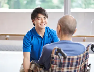 介護職員と入居者が室内でコミュニケーションを取っている様子。窓からの自然光が入る明るい空間。